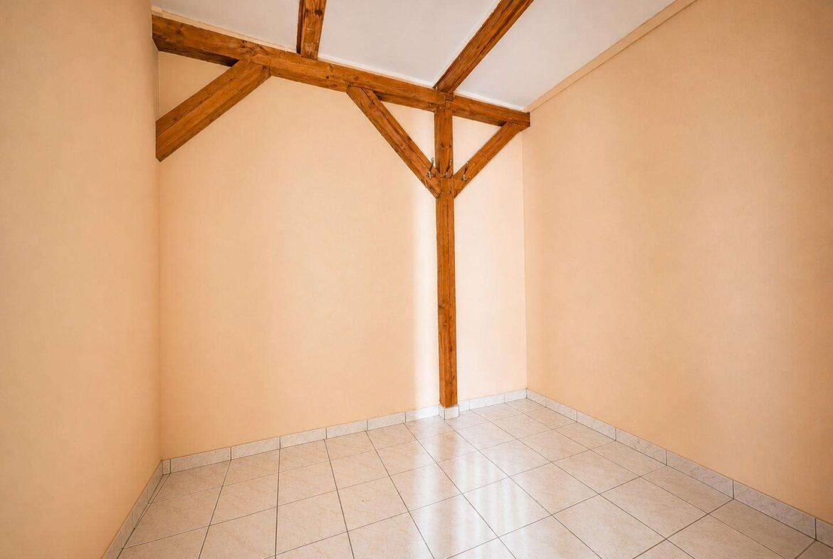 Empty corner room with peach walls, white tiled floor, and exposed wooden beams forming a triangular support in the center of the space.