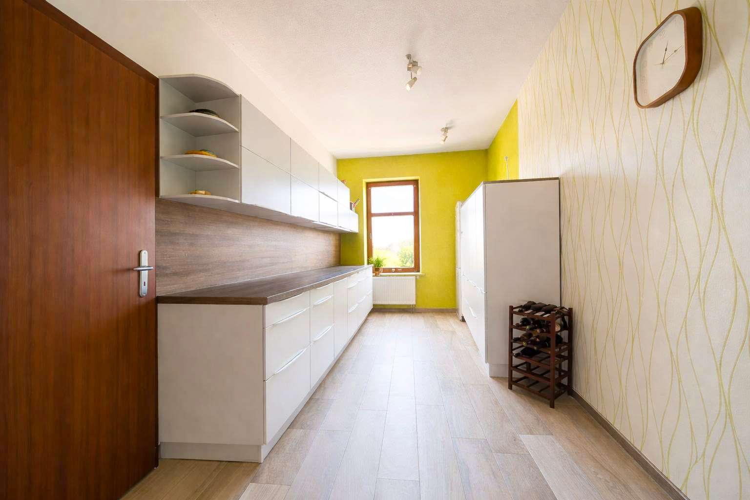 Bright modern kitchen with white cabinets, wooden countertops, and a yellow accent wall by a window.