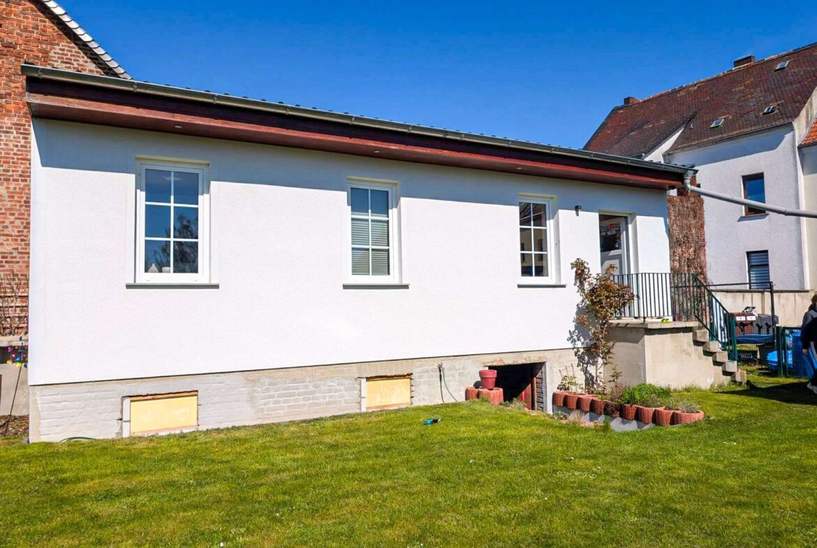 Front view of a white house with three windows, a raised entry with steps and railing, and a green lawn