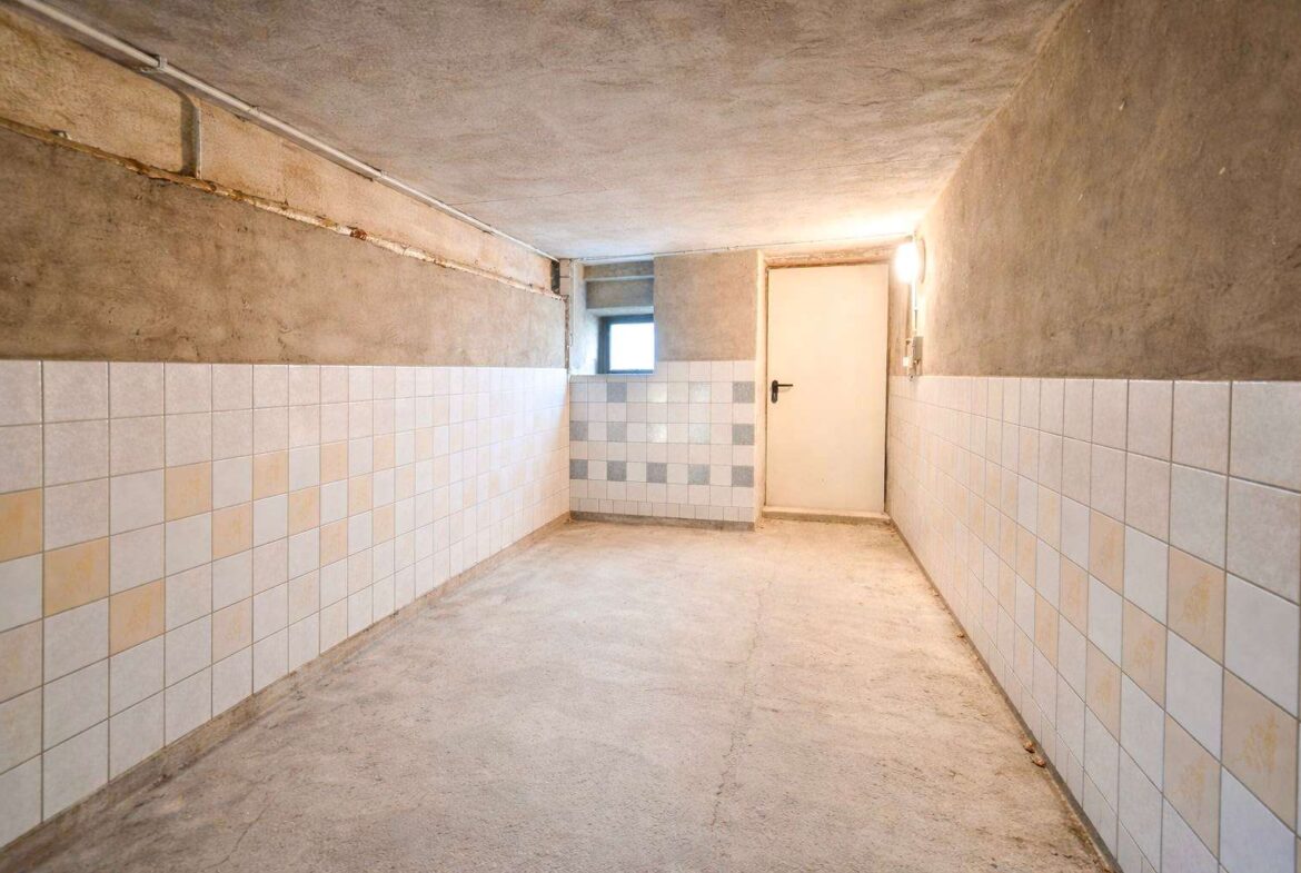 Long concrete basement corridor with tiled lower walls and a white door at the far end, small window beside it