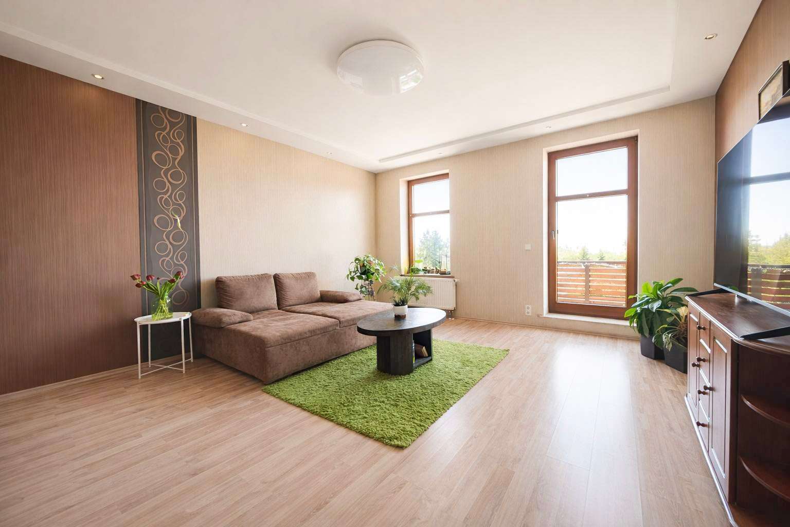 Bright living room with a brown sectional sofa on a lime-green rug, round coffee table, and potted plants. (informative)