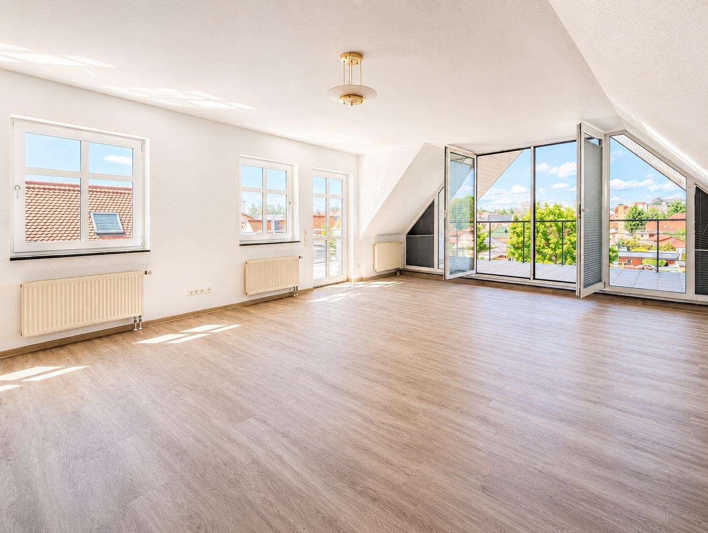 Bright empty living room with wide glass doors opening to a balcony and a sunny city view outside
