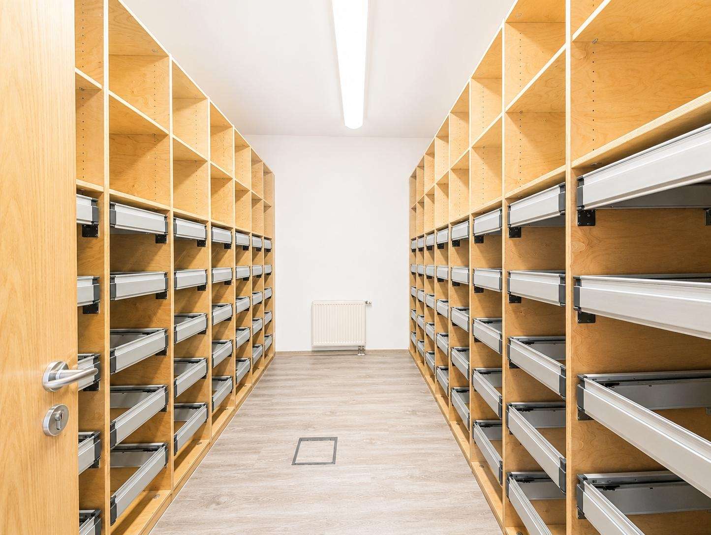 Long aisle of wooden shelving units with metal pull-out drawers in a bright storage room, clean and organized.