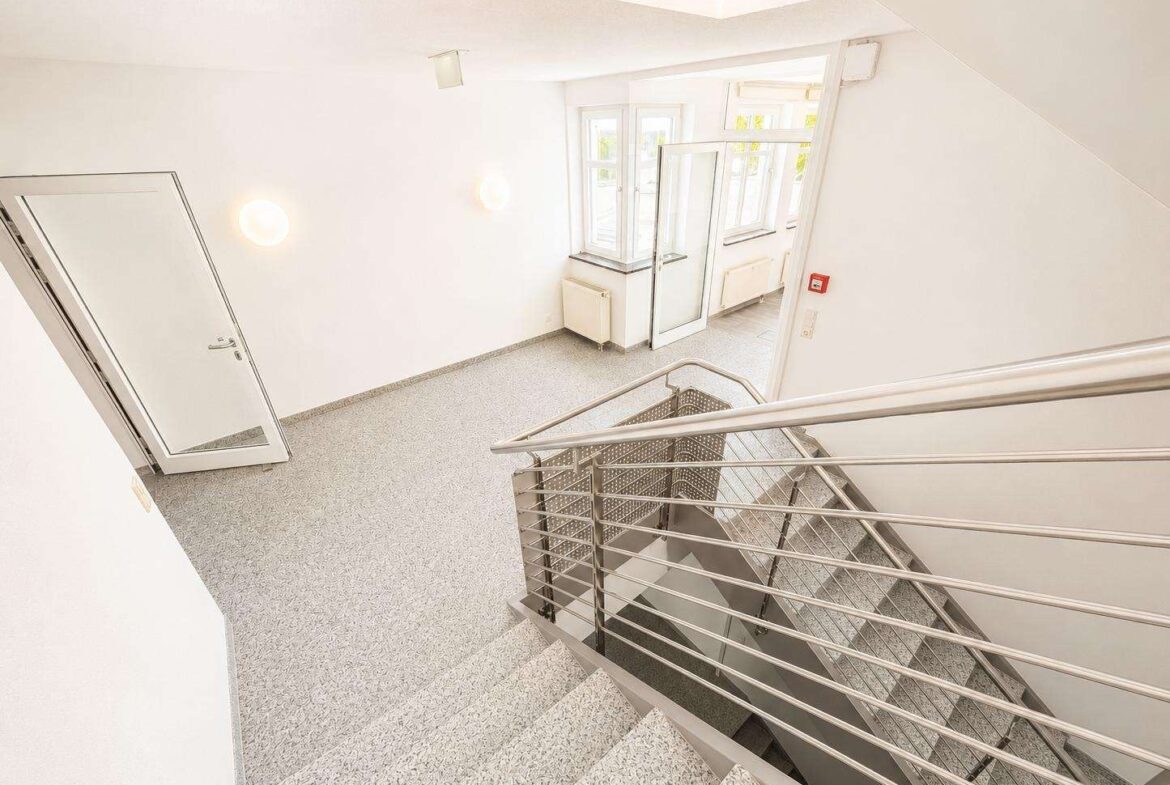Bright white stairwell with a metal railing, leading down, in a modern building near a glass door and large windows