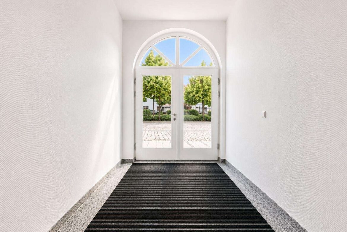 Arched glass door at end of bright hallway leading to a tree-lined outdoor scene.