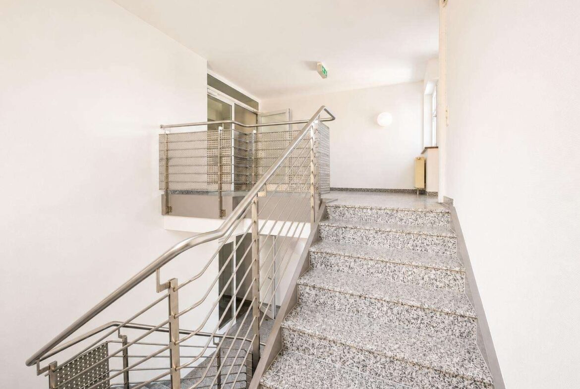 Interior stairwell in a modern building: metal railing, granite steps, white walls, and a small landing area.