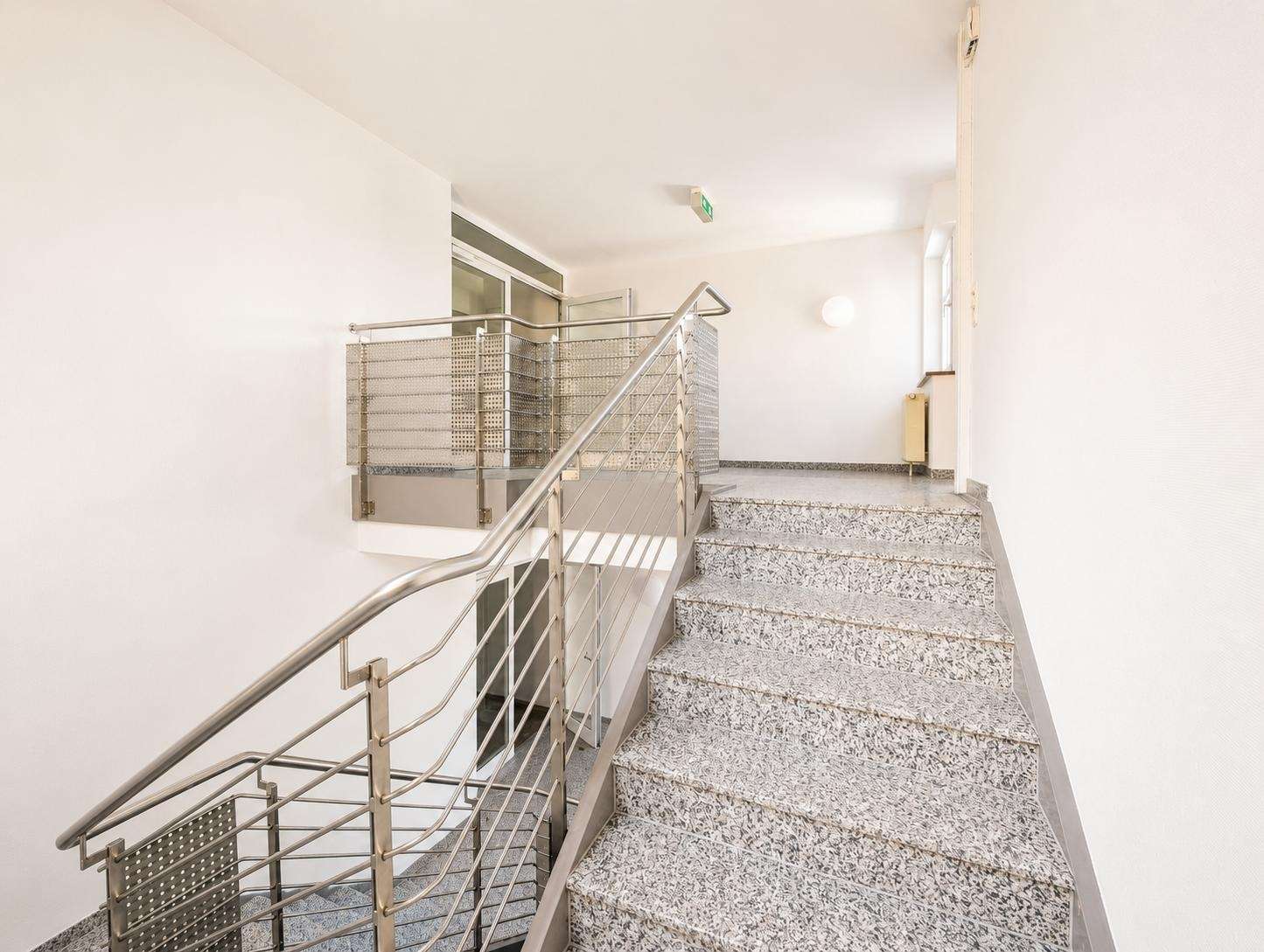 Interior stairwell in a modern building: metal railing, granite steps, white walls, and a small landing area.