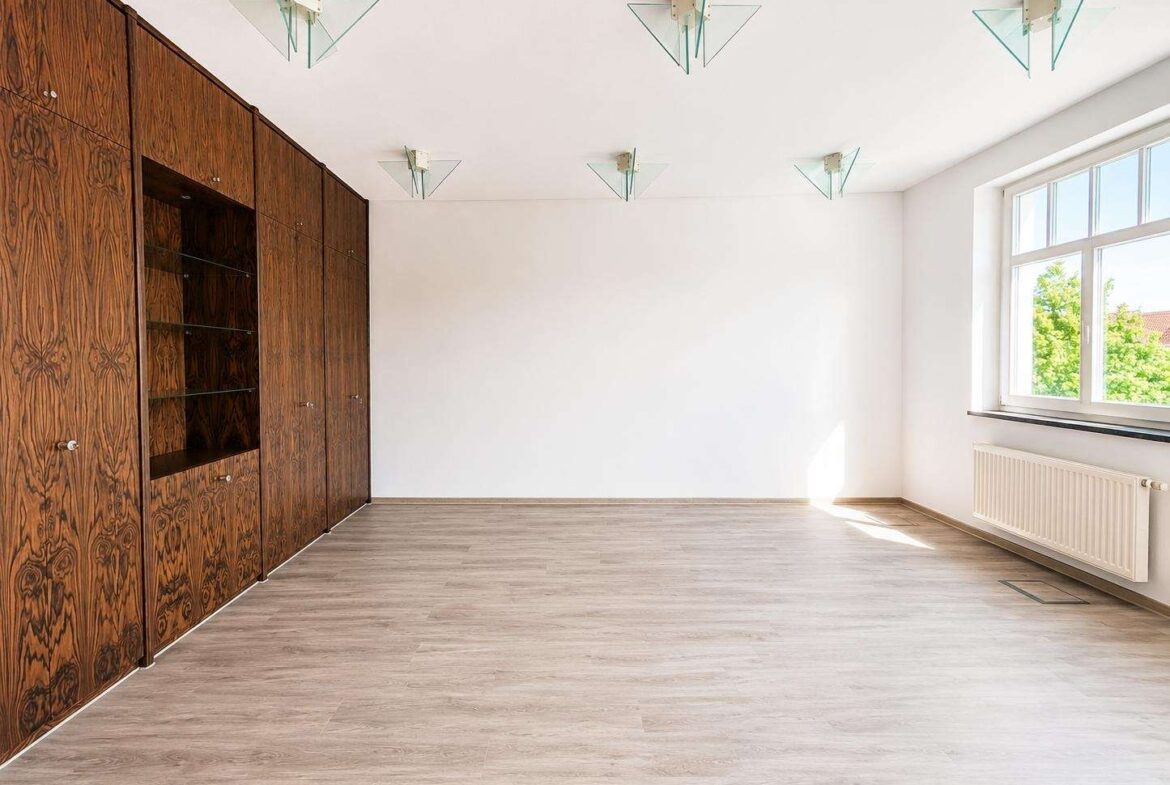 Empty room with dark wood built-in wall cabinets on the left, large window on the right, and sunlight on the floor.