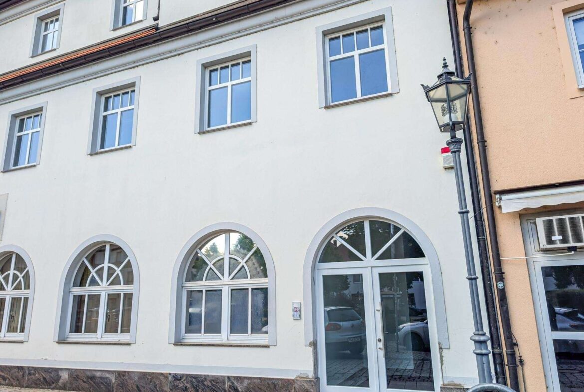 White building facade with large arched ground-floor windows and a glass door, street lamp on the right.