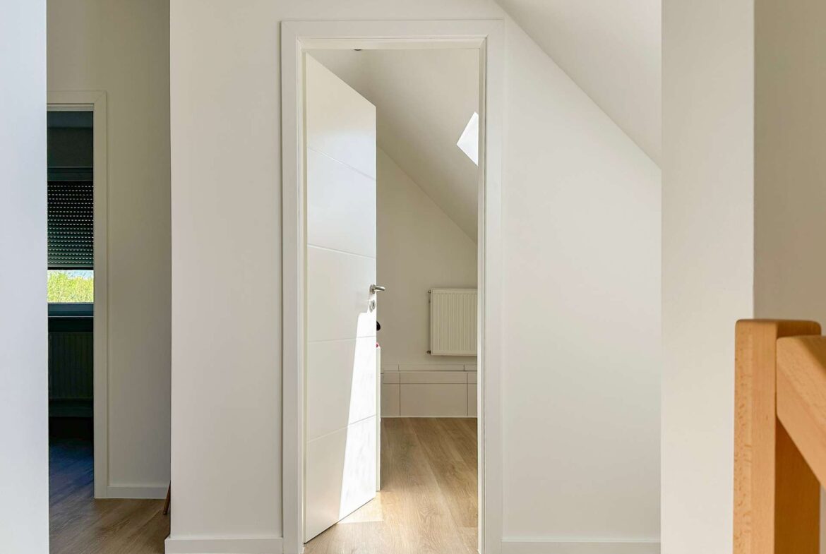 Open white door reveals a hallway with a slanted ceiling, skylight, and radiator in view.