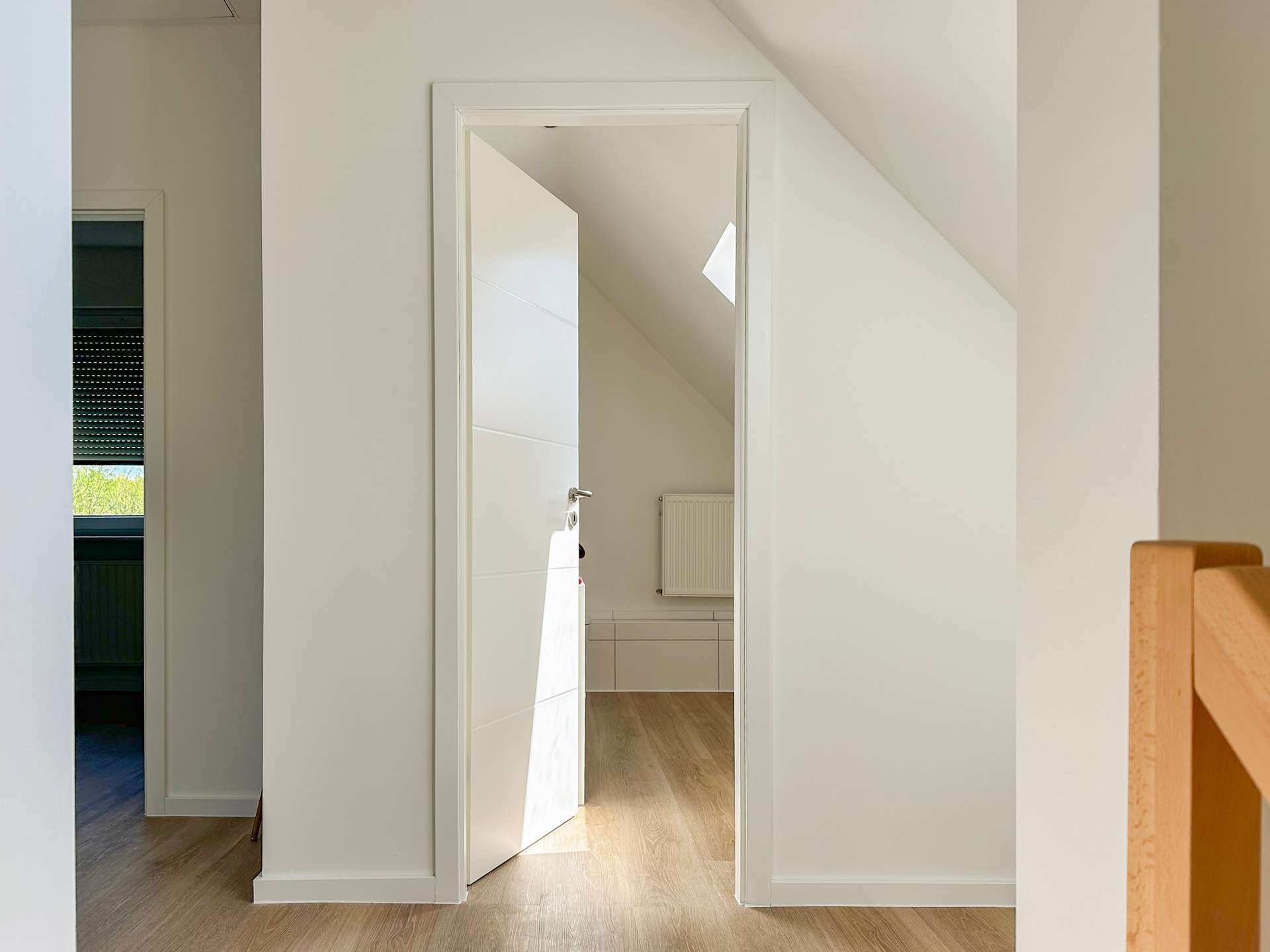 Open white door reveals a hallway with a slanted ceiling, skylight, and radiator in view.
