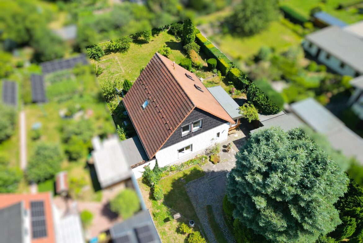 Aerial view of a house with a red-tiled roof, surrounded by a green lawn and trees.