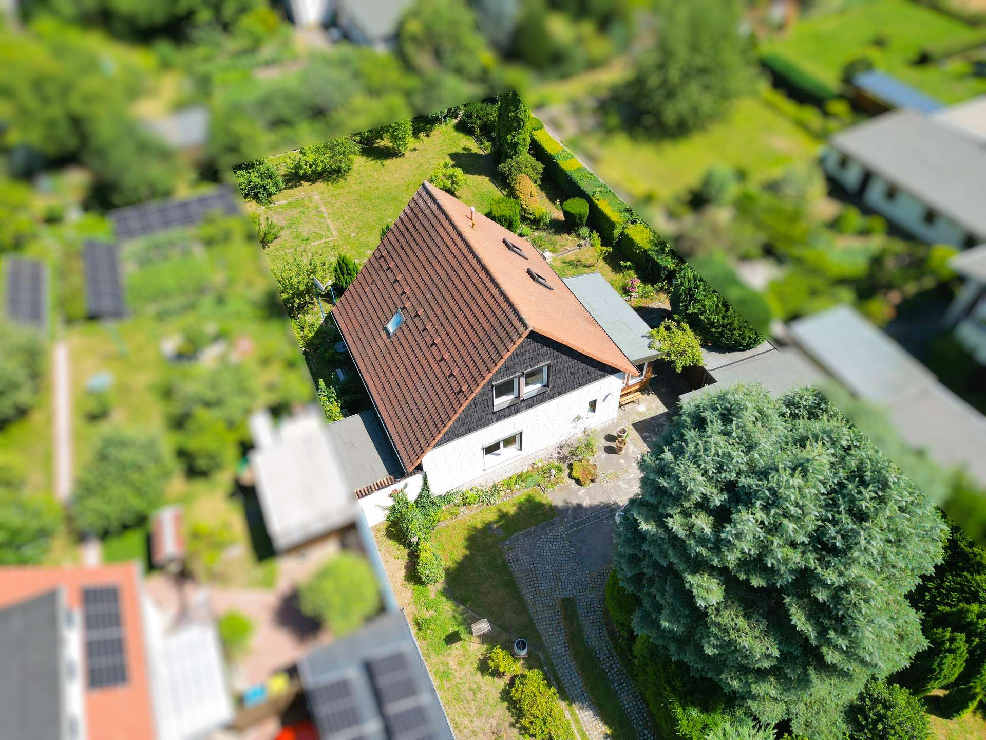 Aerial view of a house with a red-tiled roof, surrounded by a green lawn and trees.