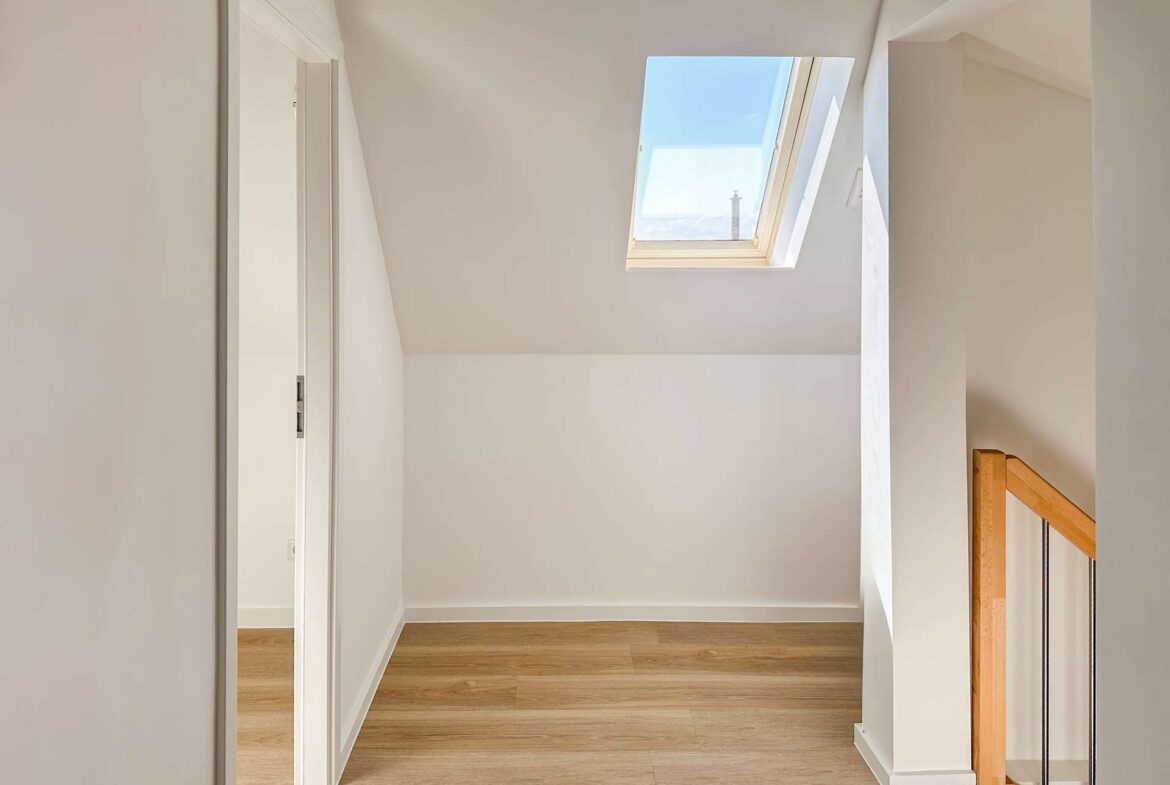 Bright stair landing with skylight window in a sloped ceiling and a wooden handrail on the right.