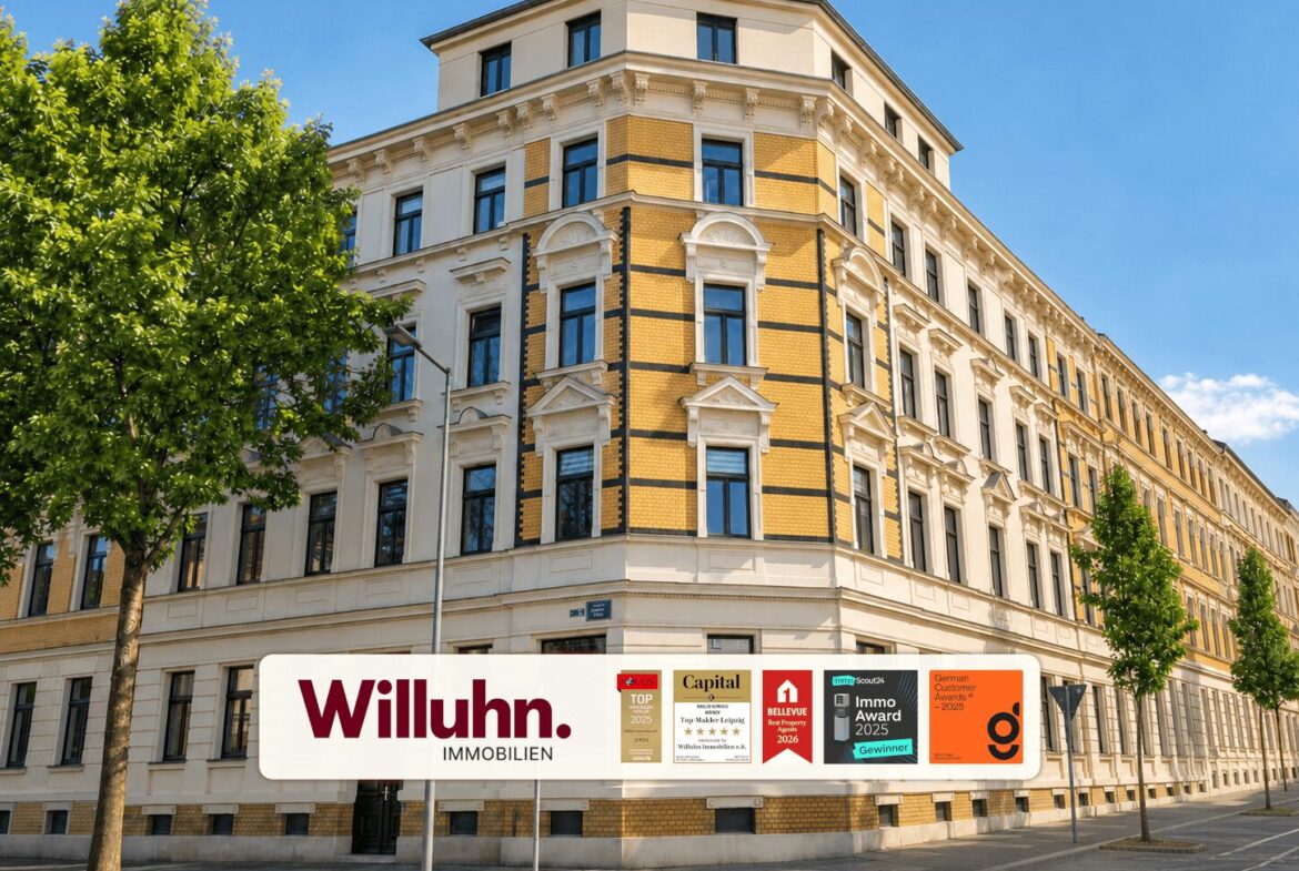 Corner building with yellow brick and white decorative trim on a sunny street; large Willuhn Immobilien banner along the sidewalk.
