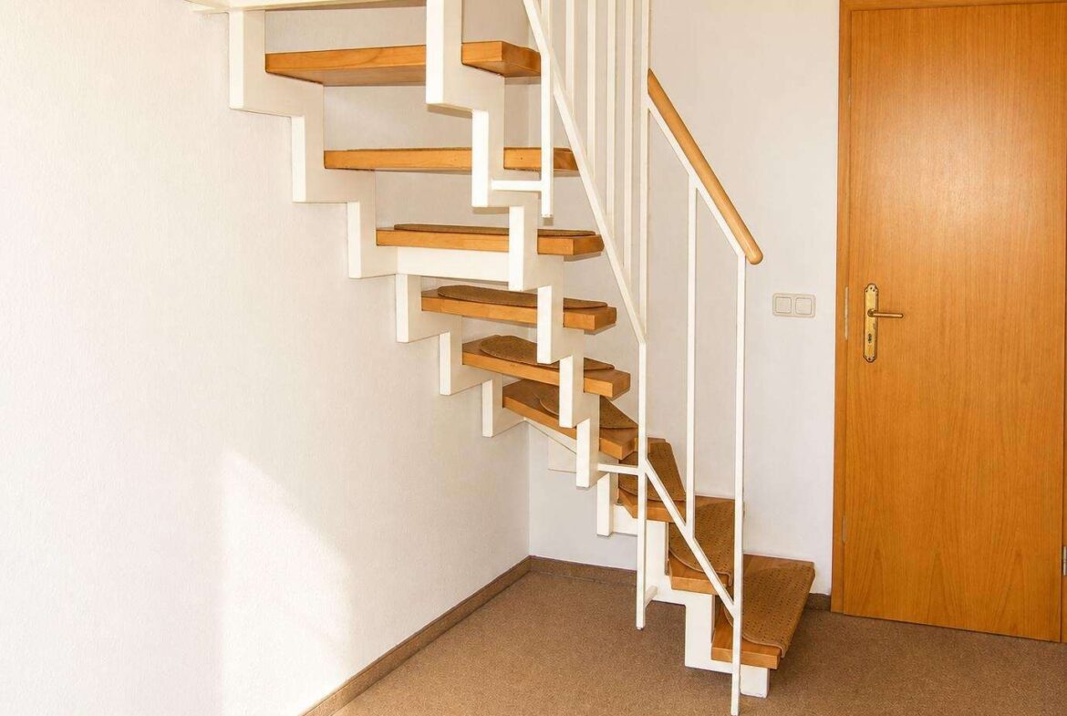 Indoor stairwell with floating cantilevered wooden steps and white metal frame, adjacent to a wooden door.