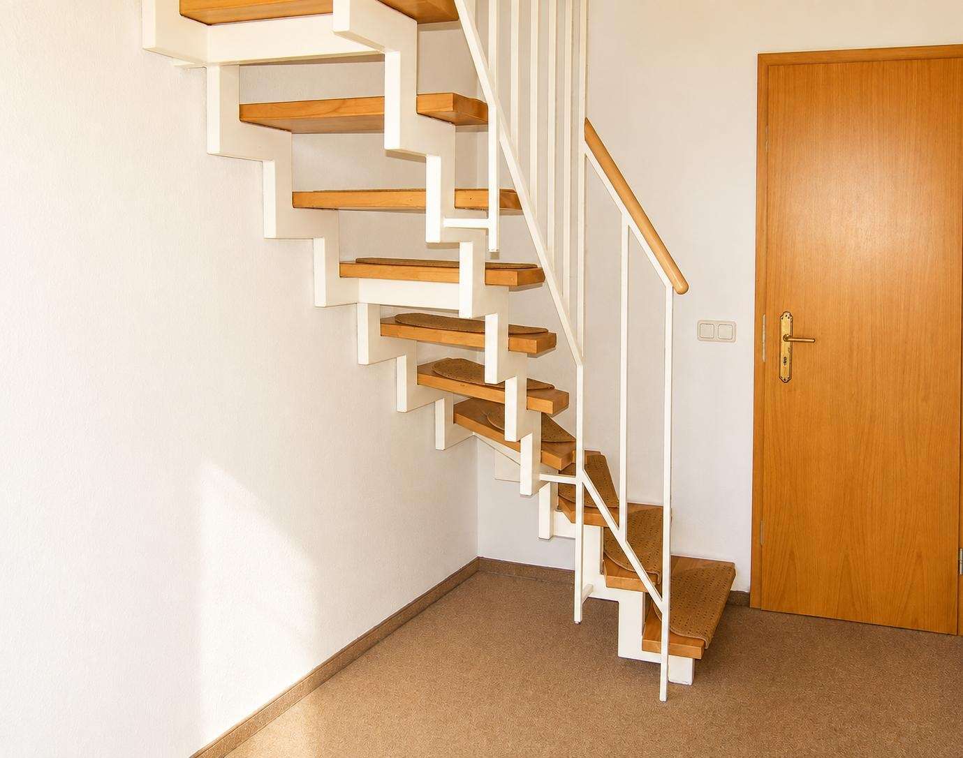Indoor stairwell with floating cantilevered wooden steps and white metal frame, adjacent to a wooden door.