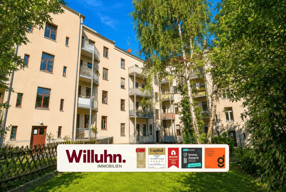 Beige apartment building with balconies, green lawn and trees, foregrounded by a Willuhn Immobilien sign with awards on it.