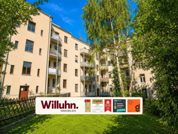 Beige apartment building with balconies, green lawn and trees, foregrounded by a Willuhn Immobilien sign with awards on it.