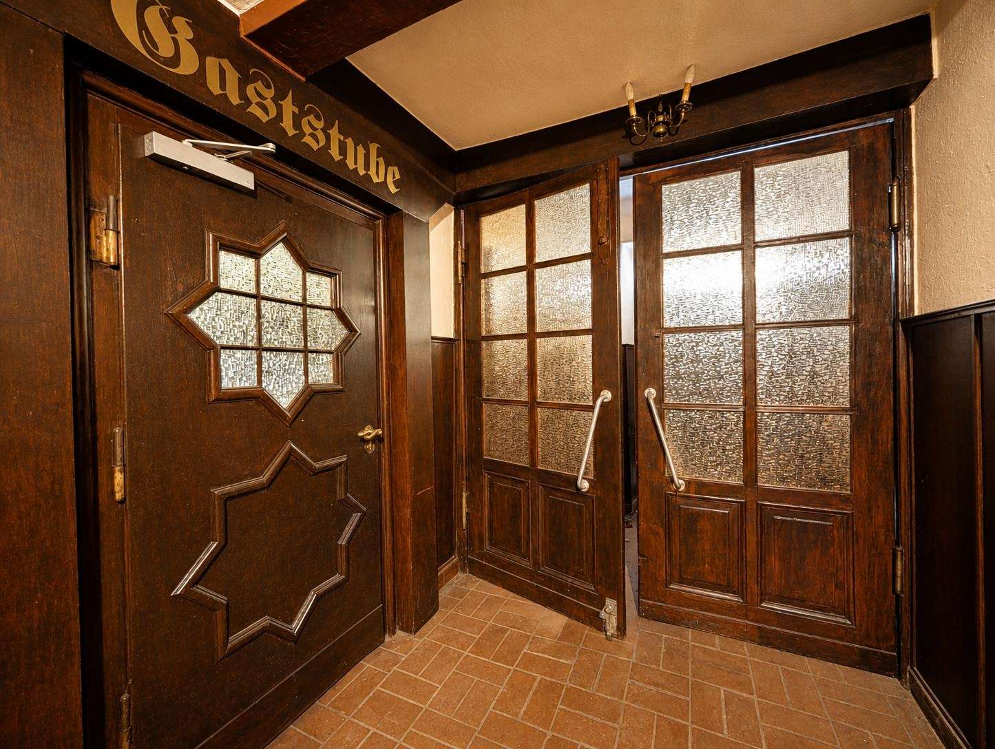 Vintage interior doorway: left door with a decorative star-like panel, right side a pair of double doors with frosted textured glass; dark wood finishes and brick floor.