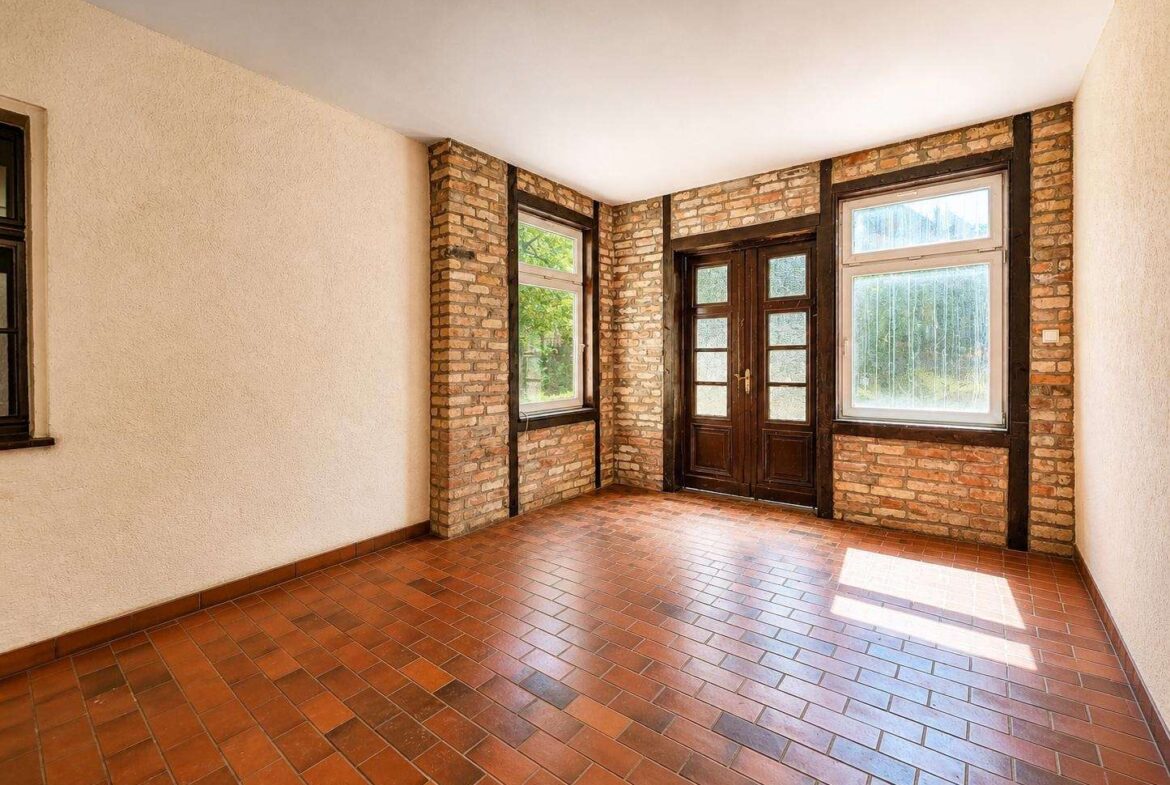 Sunlit room with exposed brick columns, dark wood-framed doors, and large windows over terracotta tile floor.