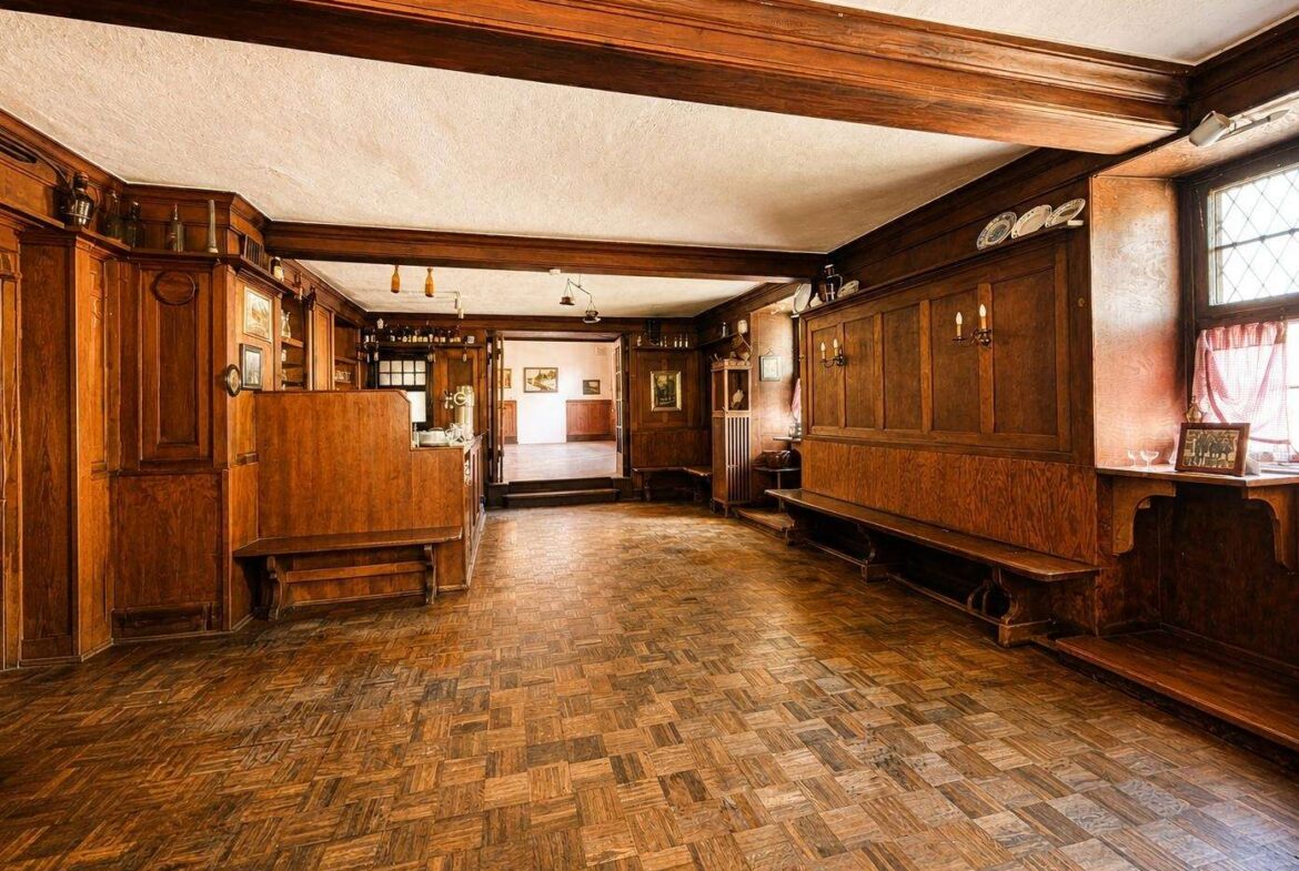 Historic wood-paneled hall with long benches, parquet floor, and warm lighting.