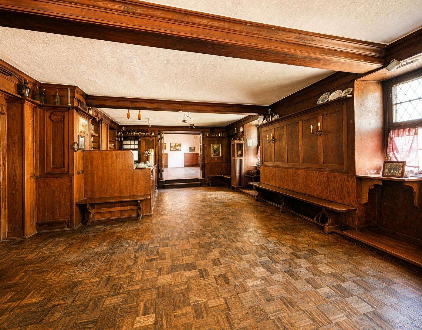 Historic wood-paneled hall with long benches, parquet floor, and warm lighting.