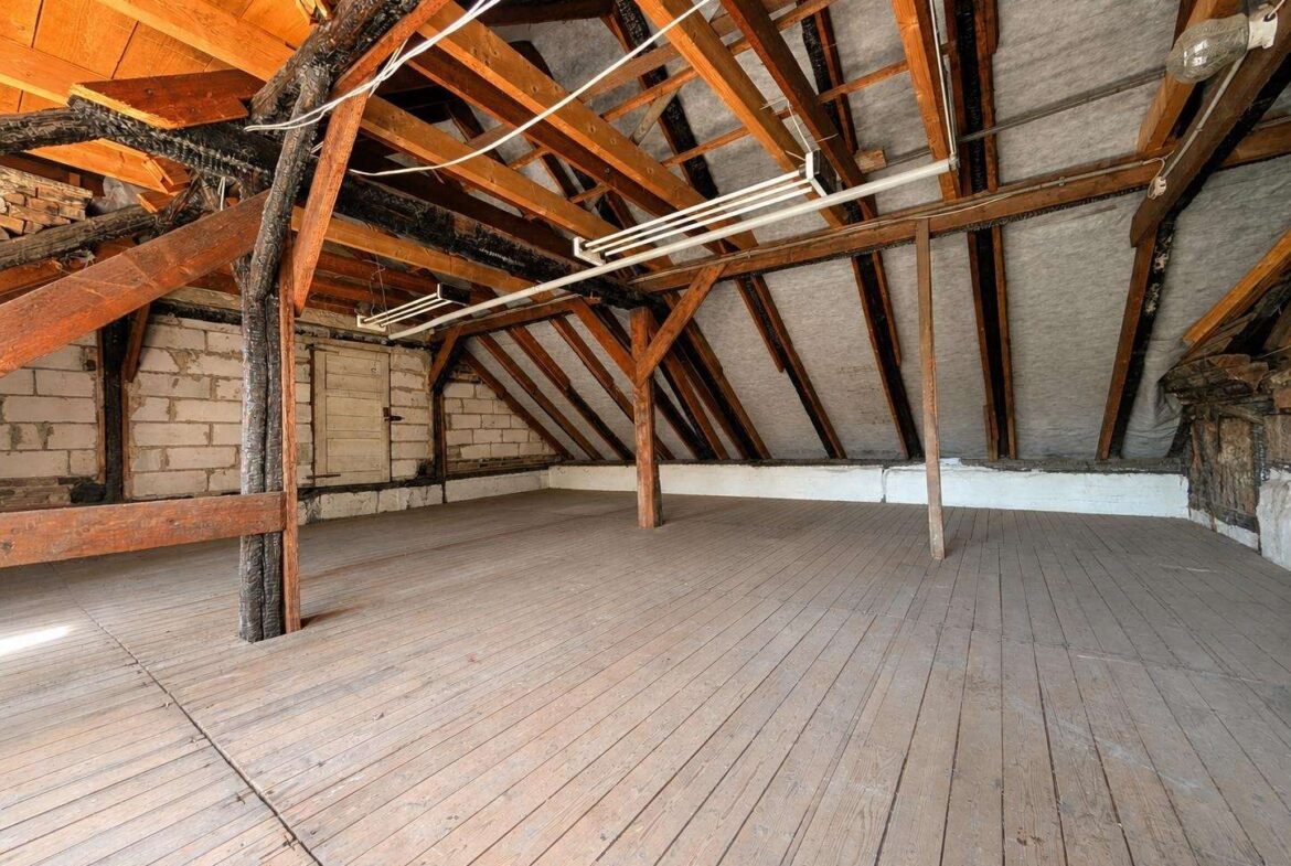Empty attic space with wooden floorboards and exposed framing, sloped roof, and support beams under insulation-covered walls and ceiling.