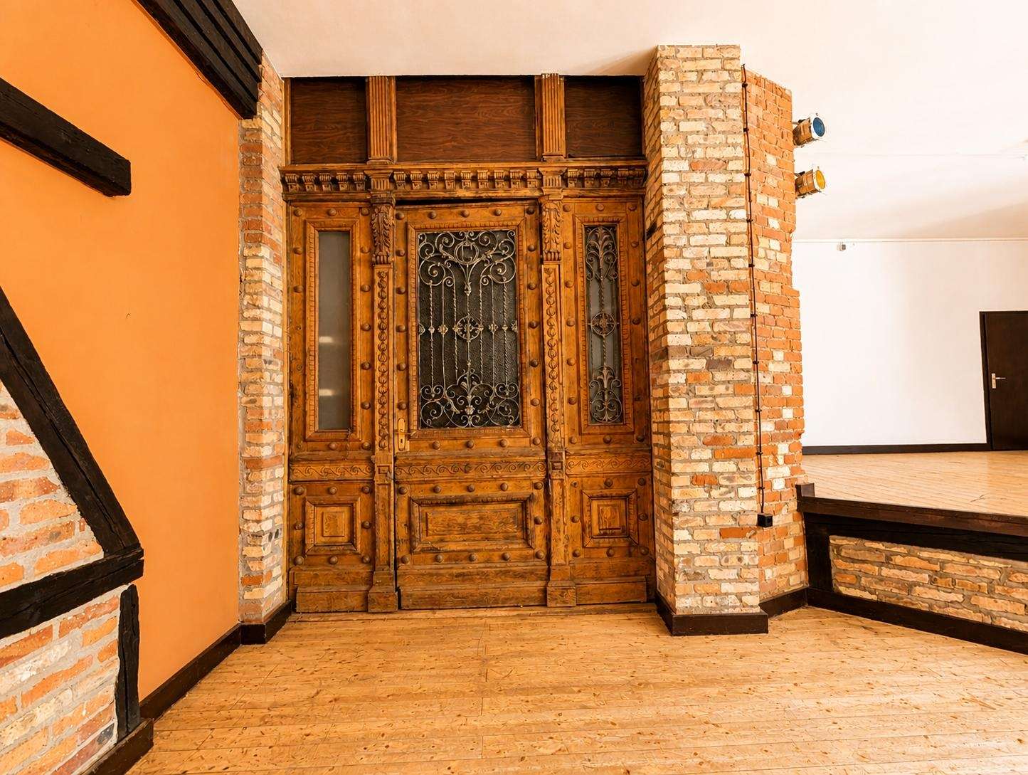 Ornate carved wooden double doors with decorative wrought-iron grille, set in brick framing inside a warm-toned room.