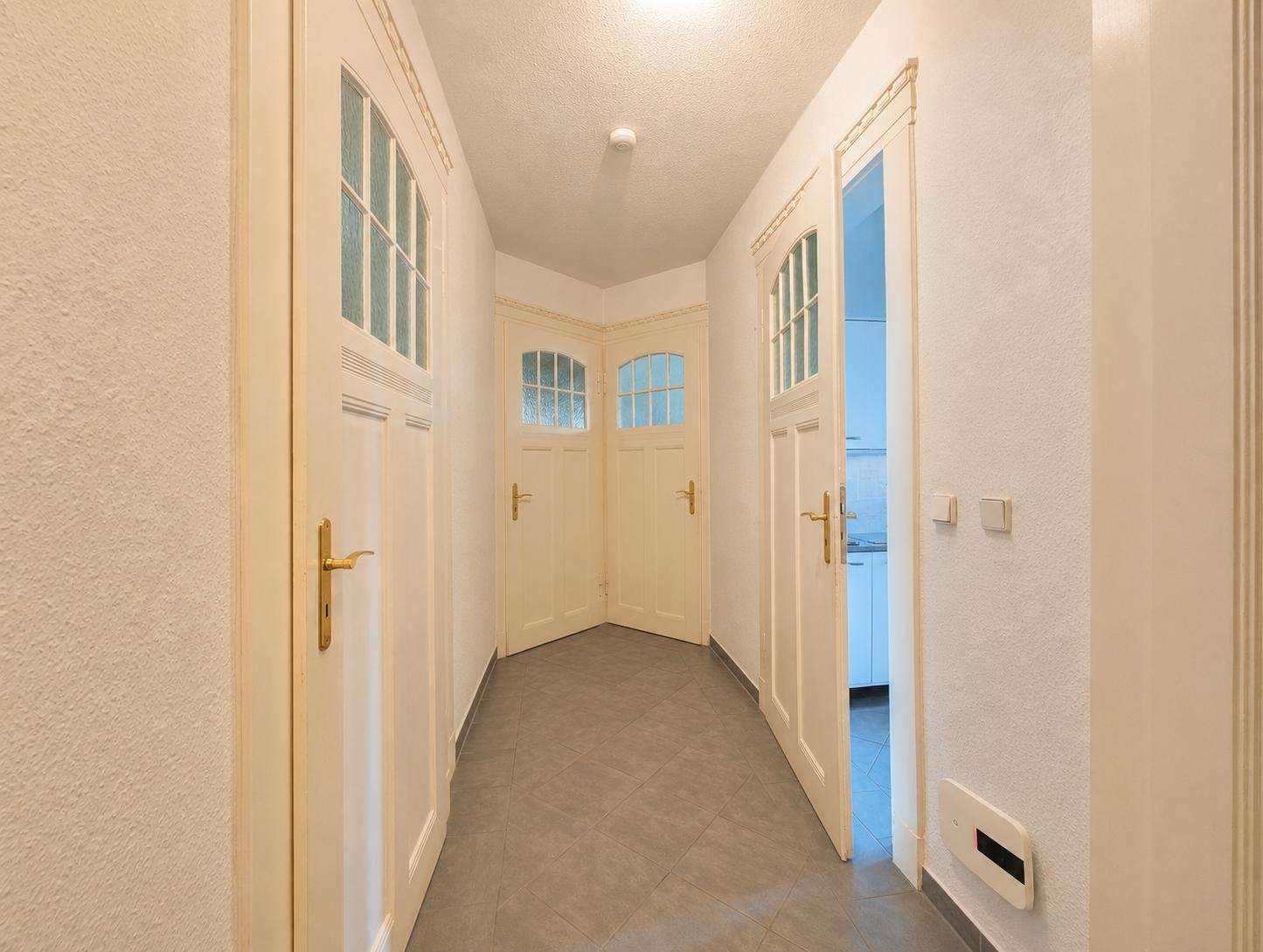 Bright hallway with white paneled doors and frosted glass windows along a tiled floor.
