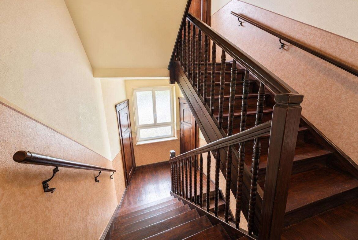 Dark wooden staircase with turned balusters and banister, set against warm beige walls, lit by a window at the landing