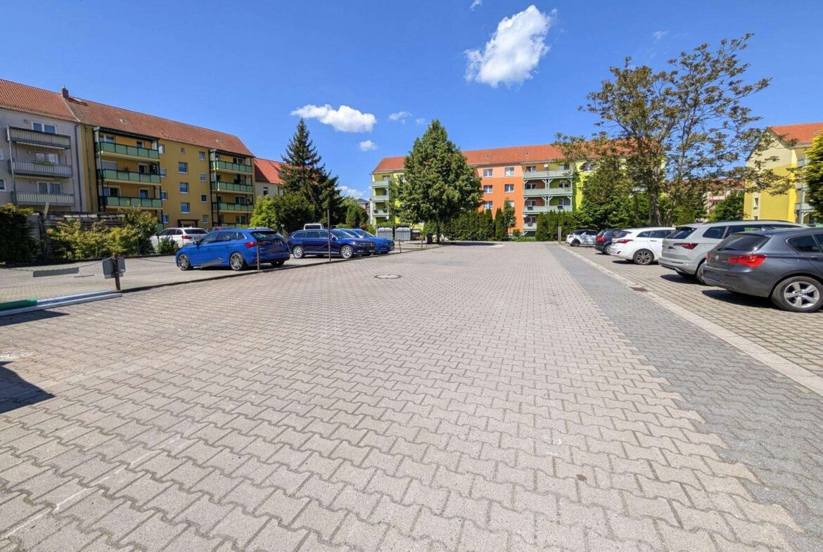 Residential parking lot with colorful apartment buildings and blue sky, cars parked along both sides.