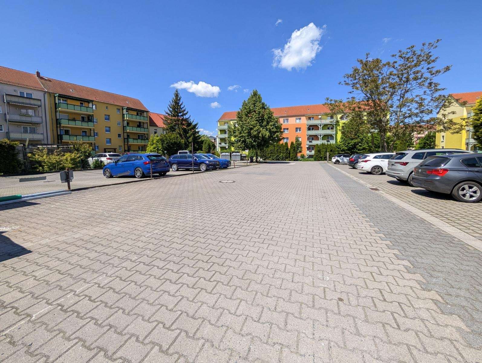 Residential parking lot with colorful apartment buildings and blue sky, cars parked along both sides.