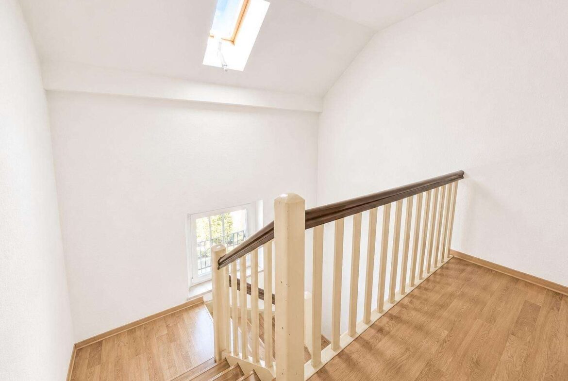 Top of a wooden staircase with a dark handrail, white balusters, and bright white walls; skylight overhead.