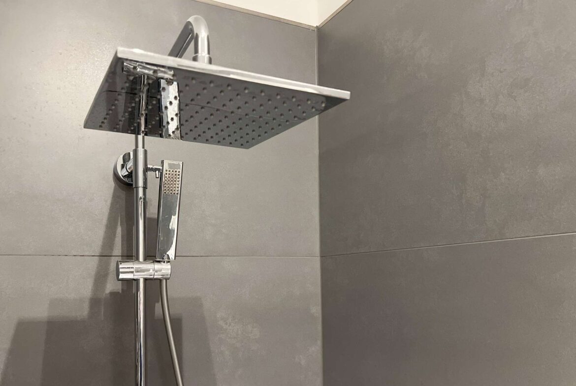 Large square rainfall showerhead with a handheld shower on a chrome rail in a modern gray-tiled shower wall