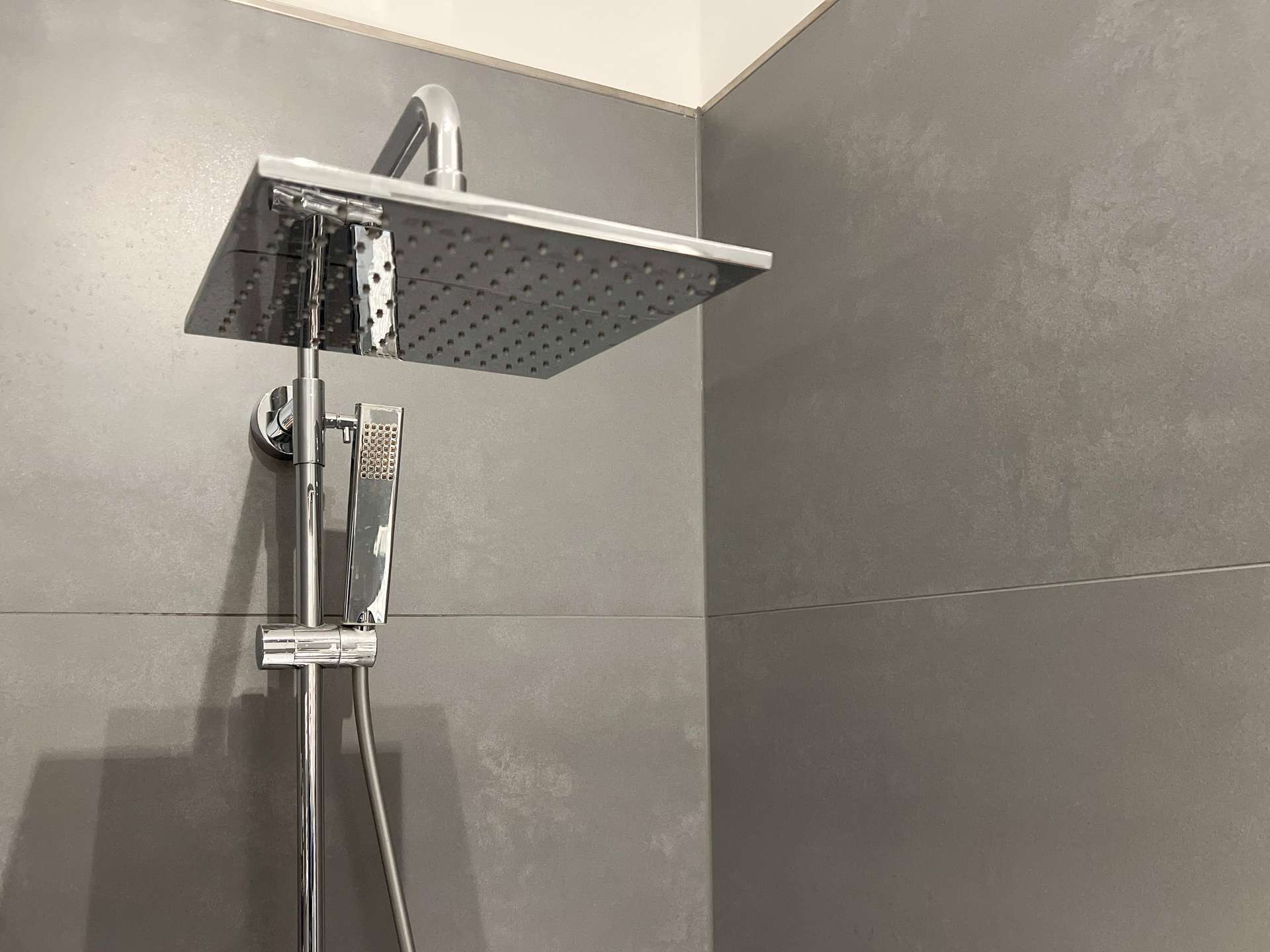 Large square rainfall showerhead with a handheld shower on a chrome rail in a modern gray-tiled shower wall