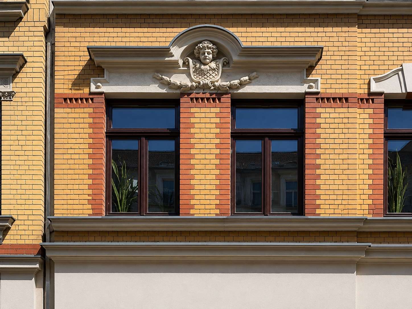 Facade of a brick building with three tall sash windows framed in dark wood; yellow and red brickwork and a decorative stone crest above the center window.