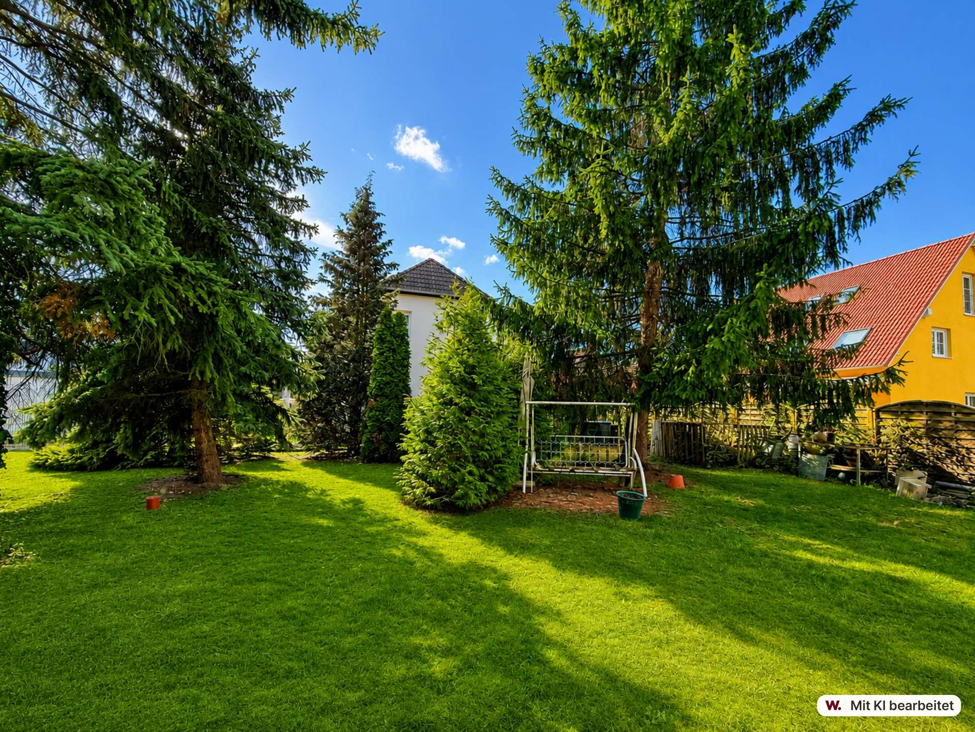 Backyard with a green lawn, tall evergreen trees, and a yellow house with a red roof under a blue sky.