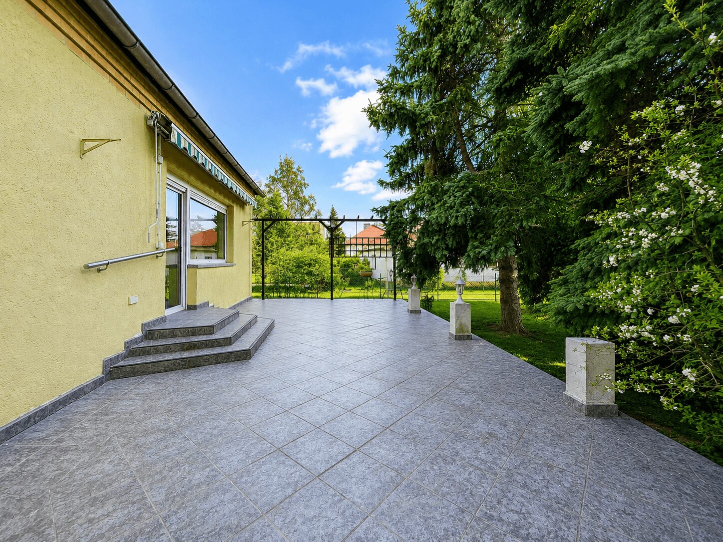 Yellow house with a tiled patio and three stone steps leading to a glass door, open garden beyond.