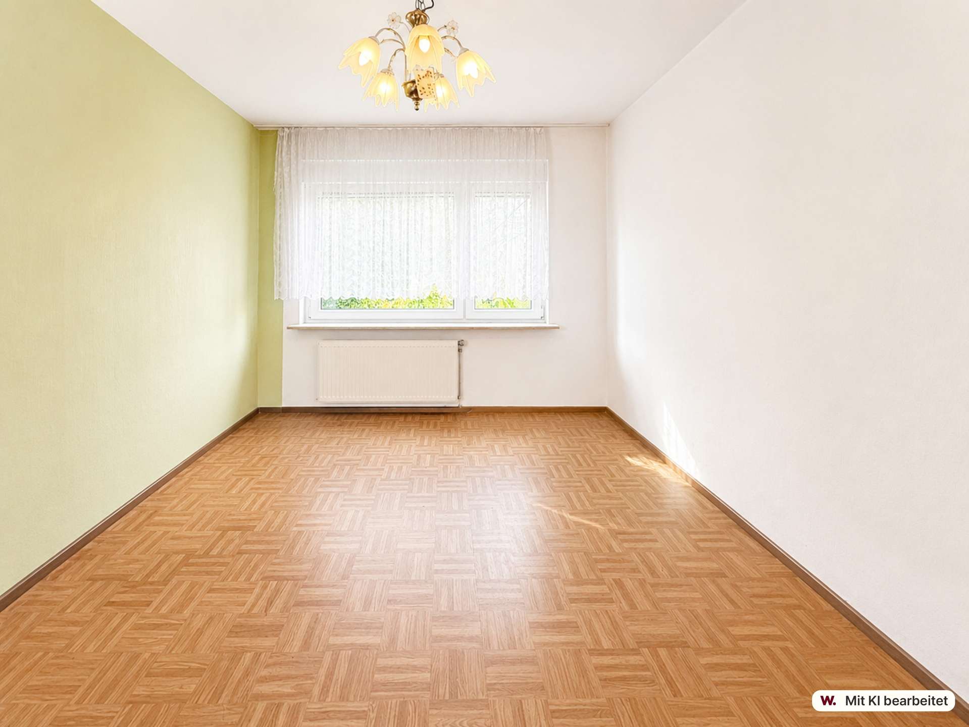 Empty rectangular room with a green left wall, white walls, a window with lace curtains, radiator beneath, and parquet floor.