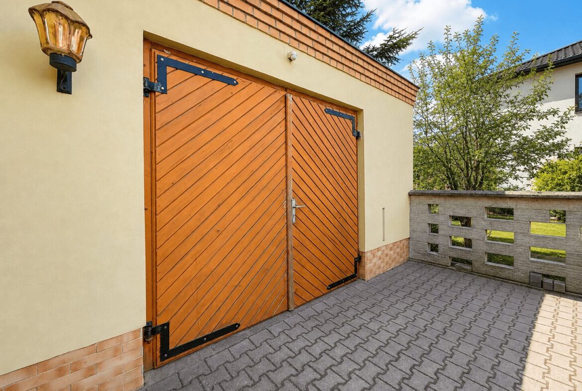 Double wooden doors with diagonal slats in a pale yellow building, brick trim, and a paved courtyard in front.