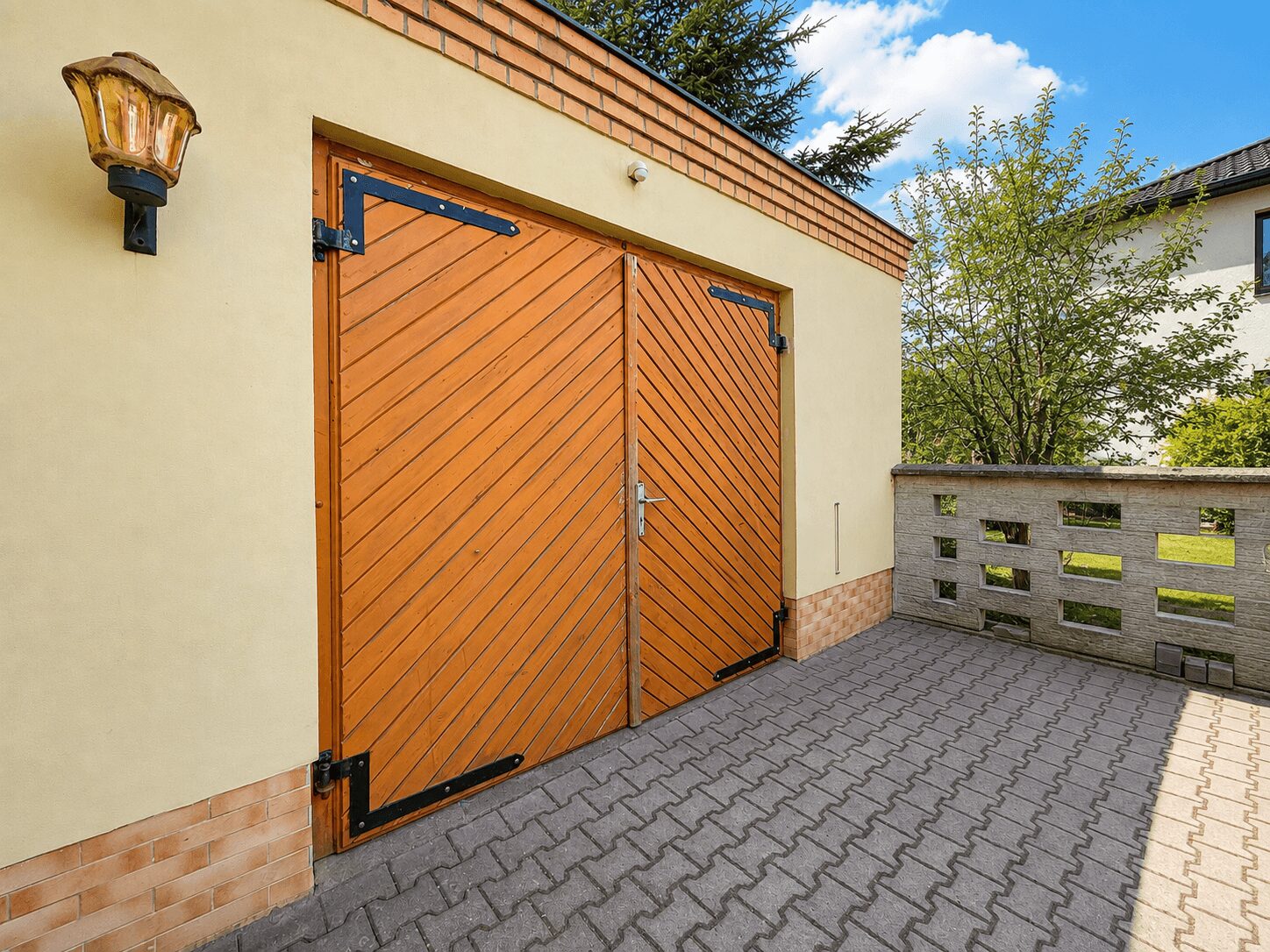 Double wooden doors with diagonal slats in a pale yellow building, brick trim, and a paved courtyard in front.