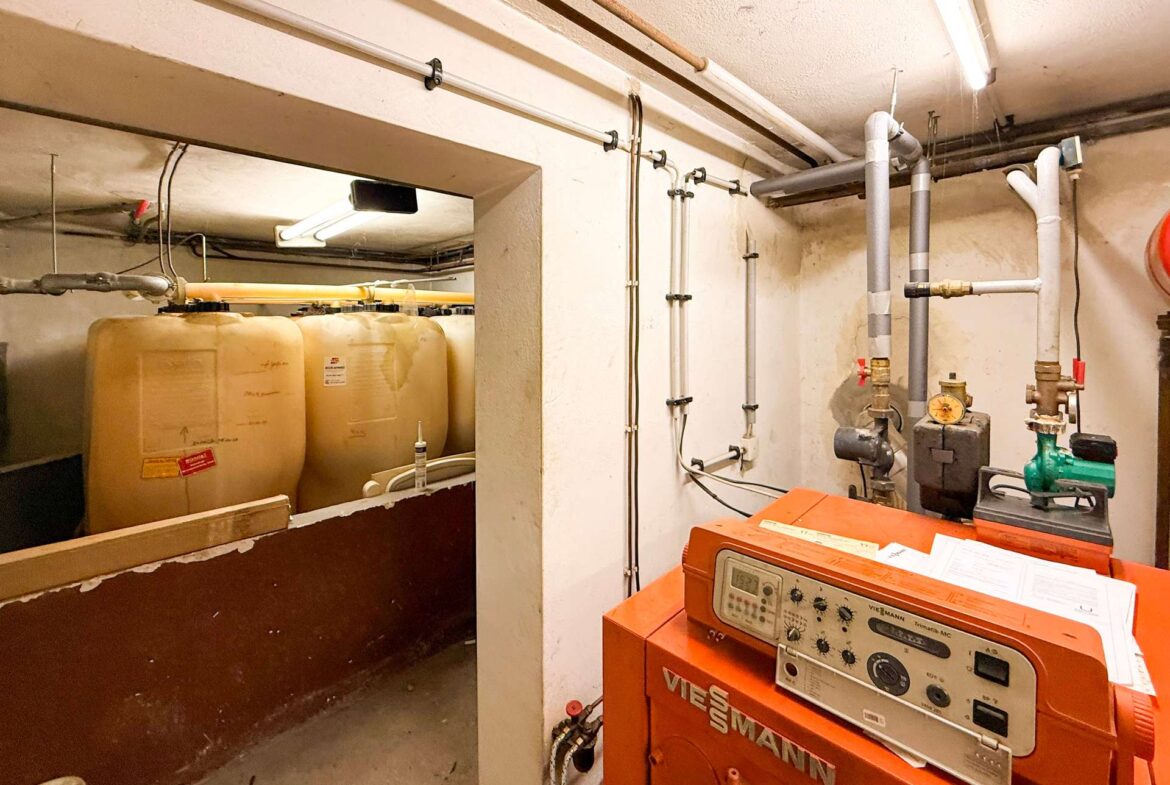 Utility room with an orange Viessmann boiler and large white water storage tanks connected by pipes along the walls, in a dim basement area.