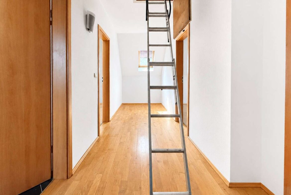 Bright hallway with wooden doors and a tall metal ladder reaching up to an attic hatch.