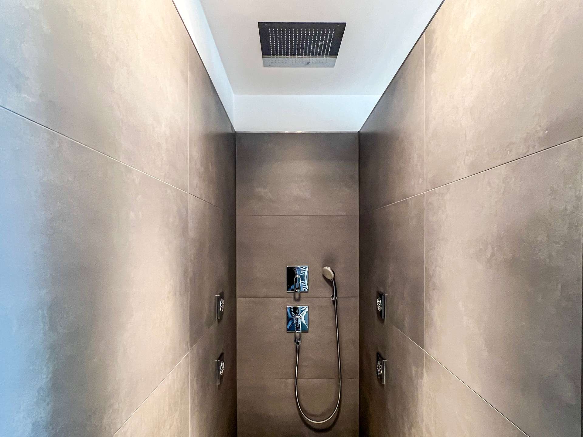 Modern gray-tiled shower enclosure with a square ceiling rain shower and a handheld shower on a wall panel.