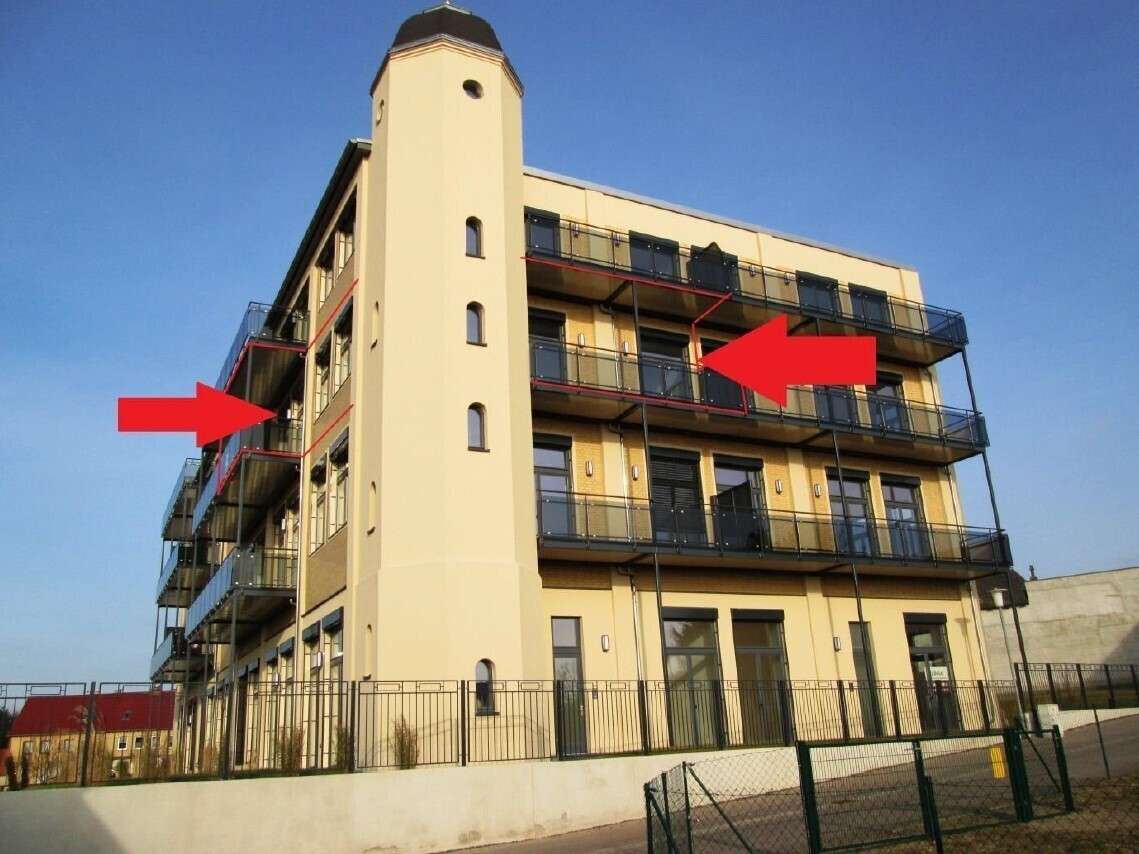 Multi-story beige apartment building with glass balconies; two red arrows point to the upper and mid-level balconies.