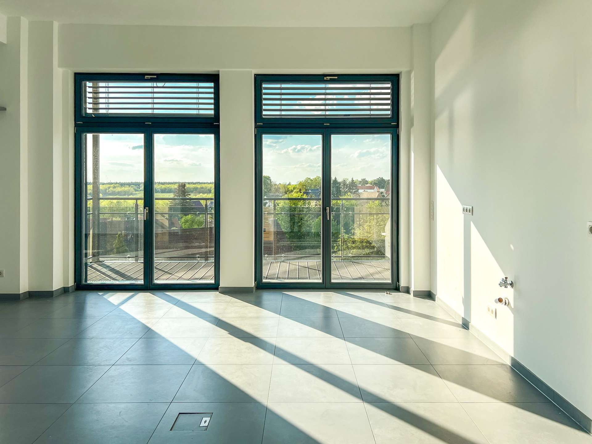 Modern empty room with large blue-framed glass doors opening to a balcony and a view of trees outside.