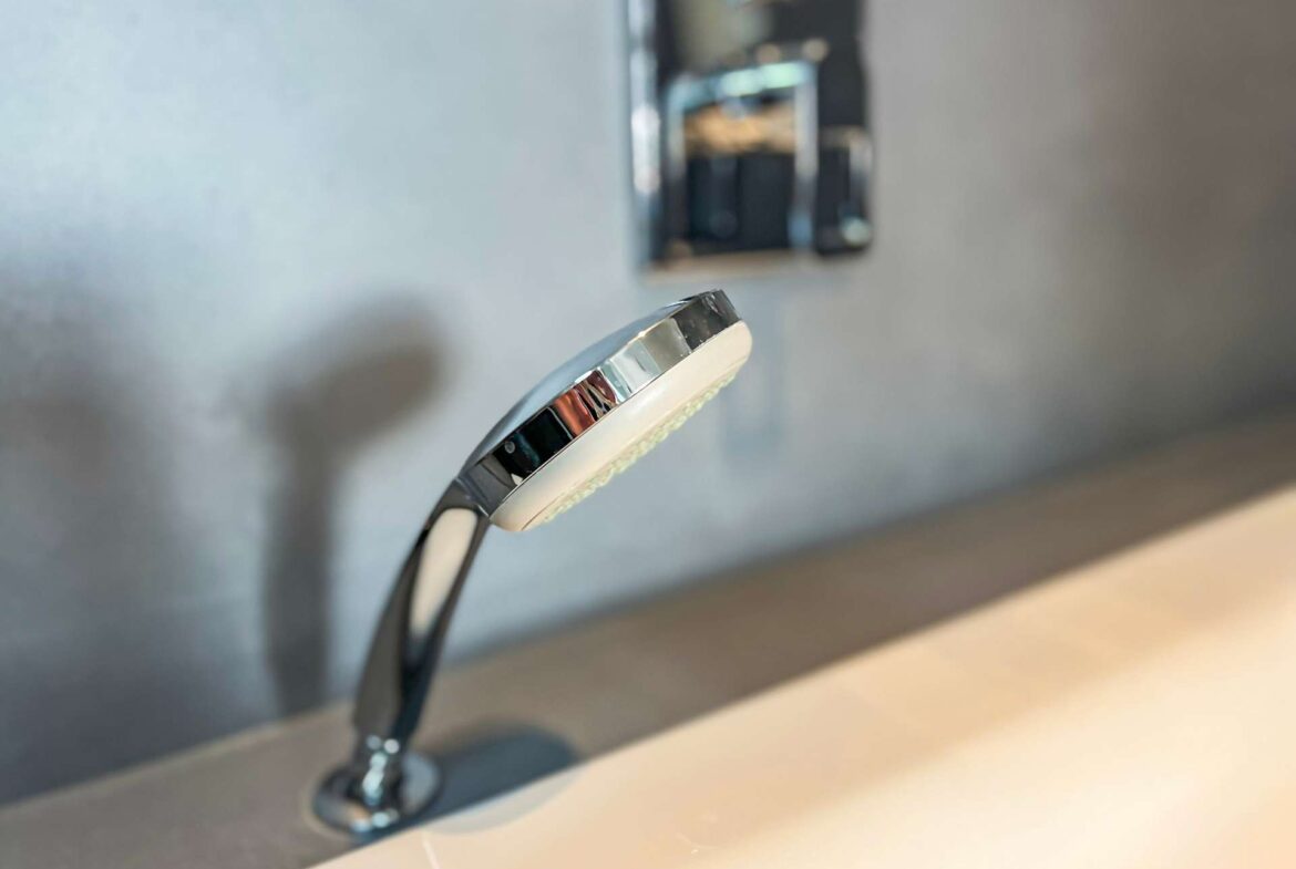 Close-up of a chrome faucet head over a sink with a blurred background, showing a sleek modern design.