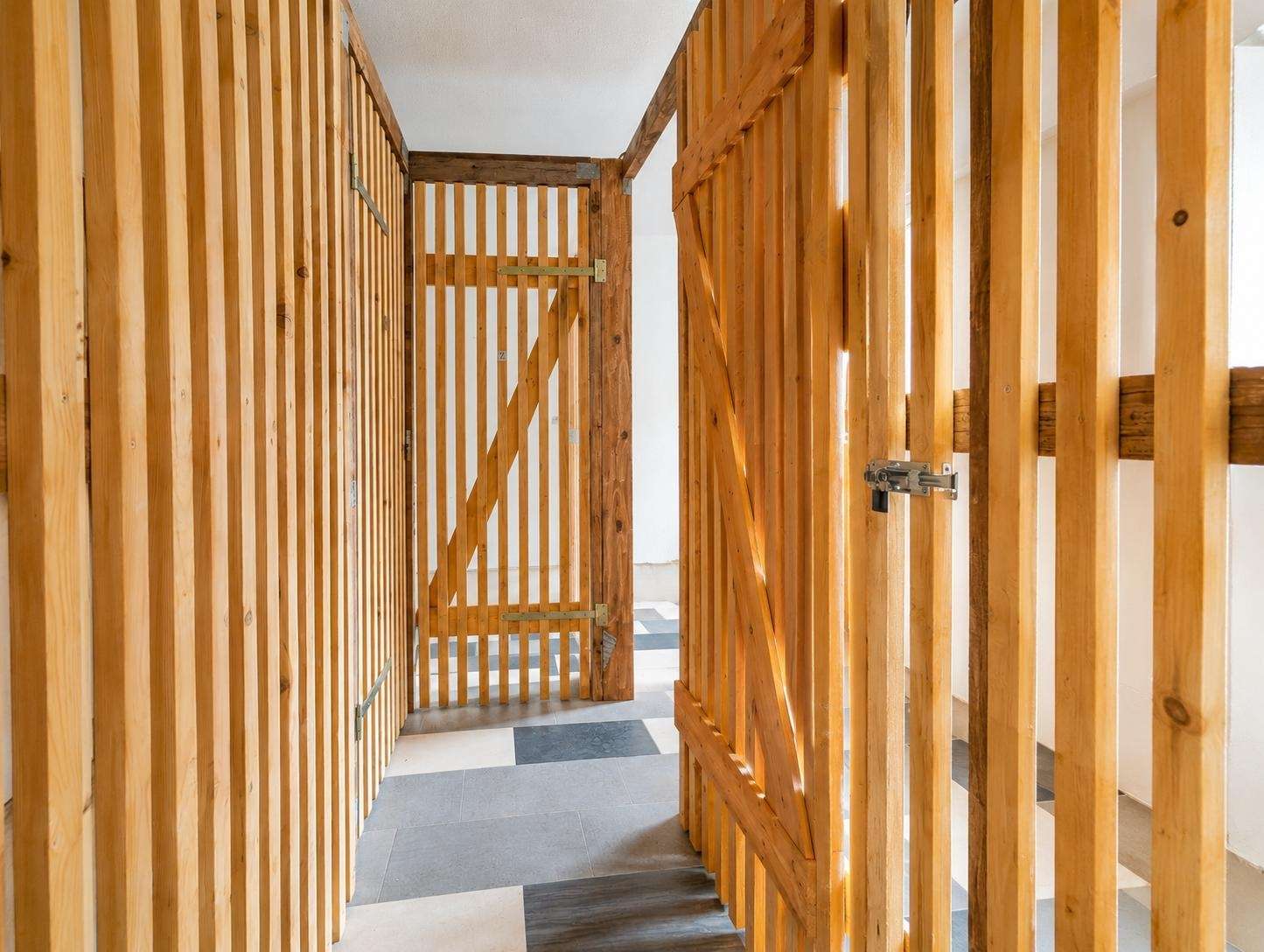 Interior hallway with vertical wooden slat partitions and a gate at the end, forming a fenced corridor.