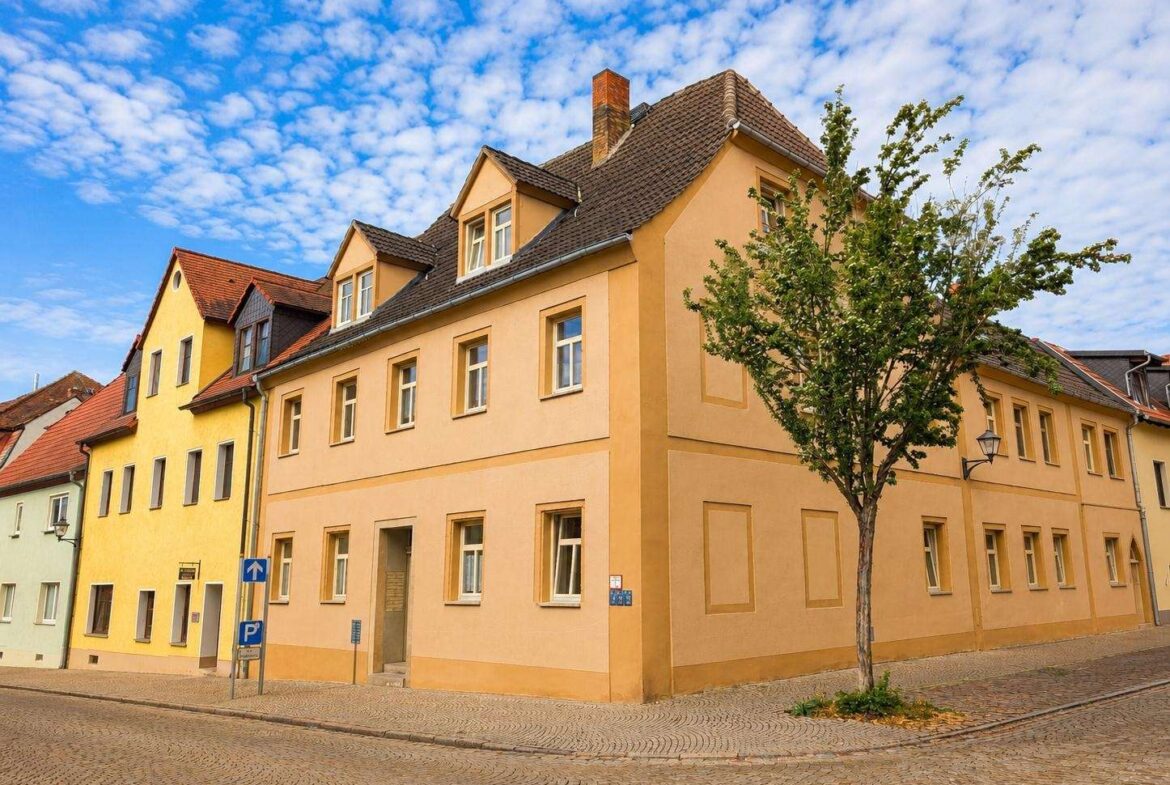 Colorful row of pastel houses on a cobblestone street with a small tree in front under a blue sky.